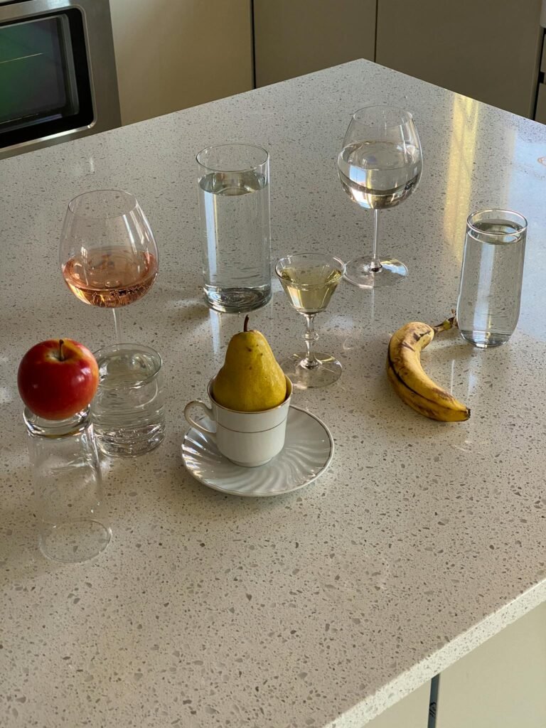 From above of fresh pear with apple and banana composed on table with various shaped glasses with different beverages in kitchen