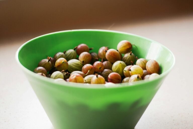 High angle of ripe gooseberries in green deep plastic bowl on table on summer day